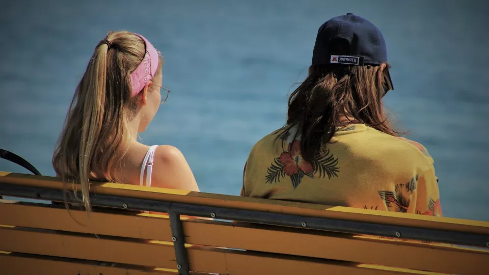 Ung kvinna och man vid strand på bänk