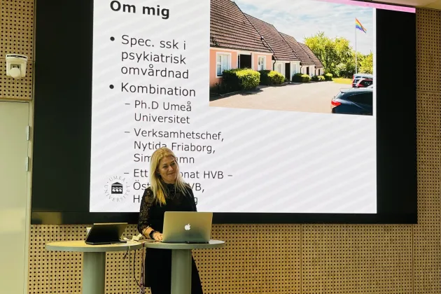 Kvinna står och föreläser framför sin powerpoint