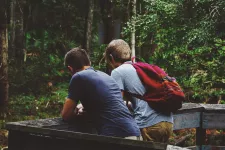 Två män ses bakifrån, lutar sig försiktigt över ett träräcke och verkar samspelta